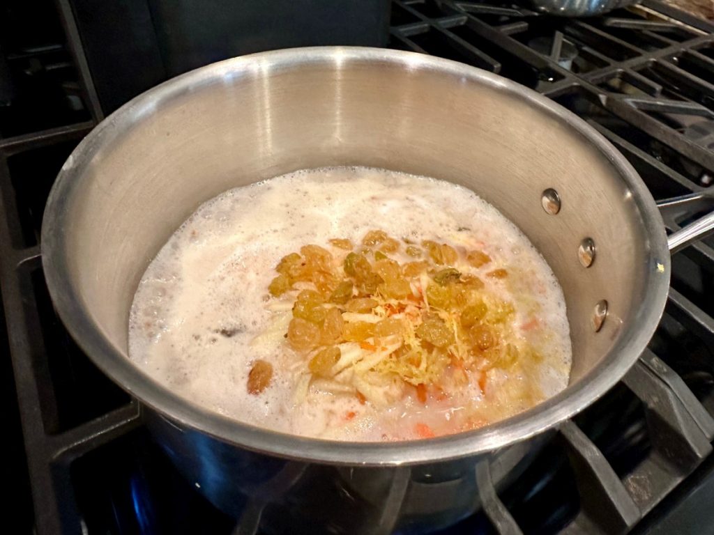 steel cut oats cooking with shredded carrots, spices, & golden raisins for healthy carrot cake oatmeal