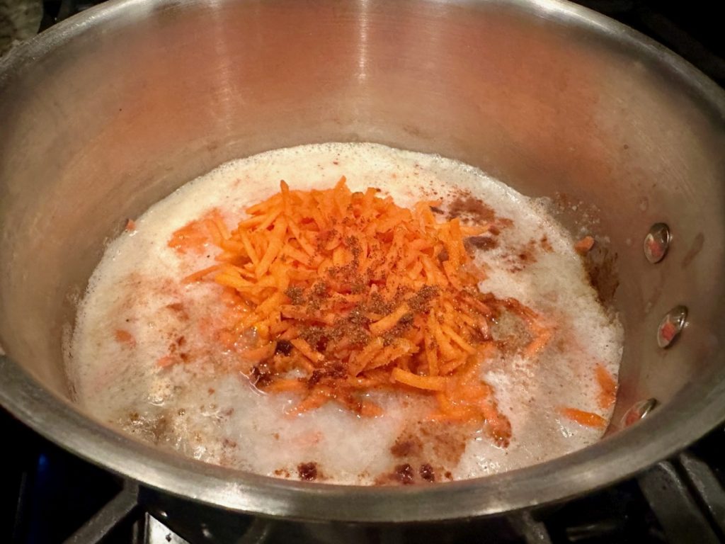 steel cut oats cooking with shredded carrots, spices, & golden raisins for healthy carrot cake oatmeal
