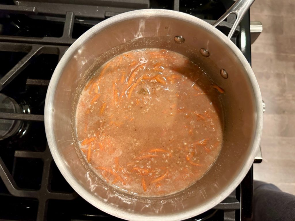steel cut oats cooking with shredded carrots, spices, & golden raisins for healthy carrot cake oatmeal